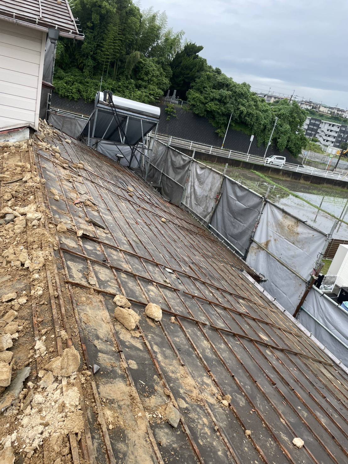 瓦を下ろし終えた屋根と、建物を囲う足場・養生シート