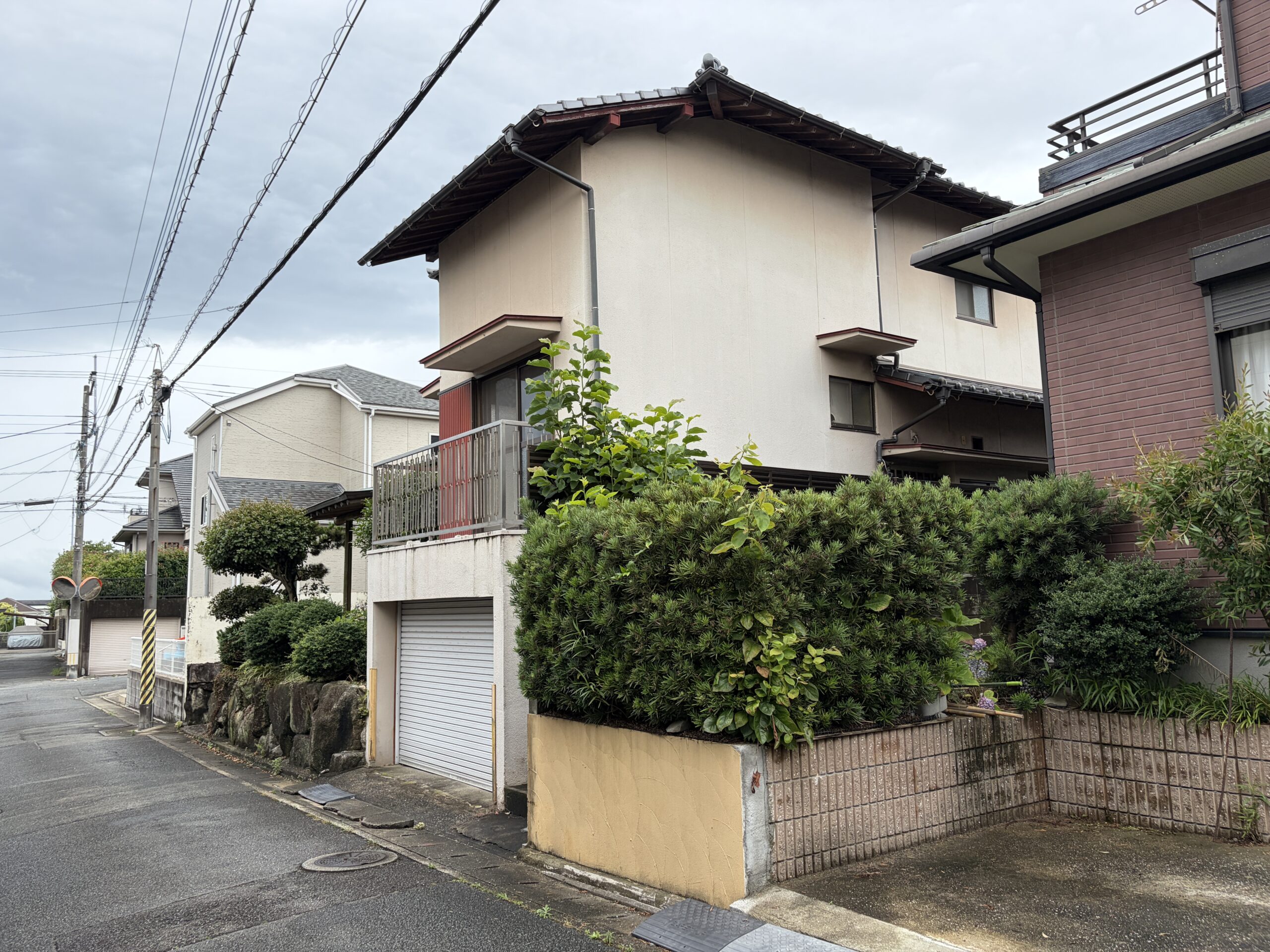 道路から見上げた、生垣と石垣に囲まれた木造2階建て住宅の全景