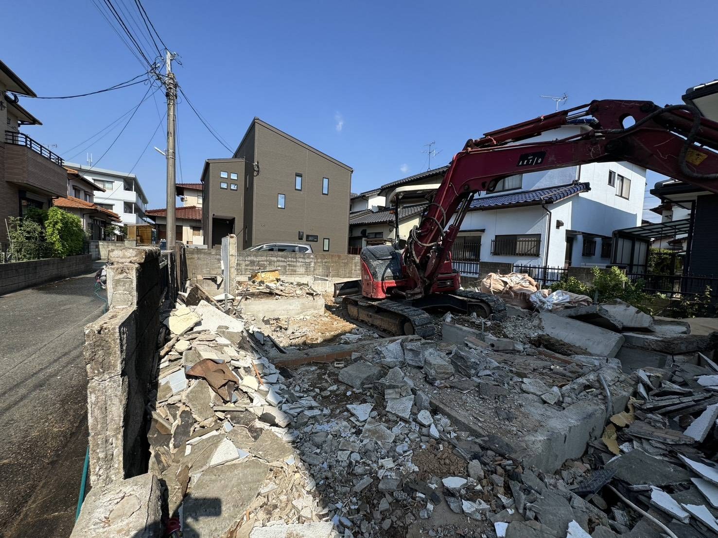 重機で基礎を割って撤去している解体現場。両側にブロック塀が迫る