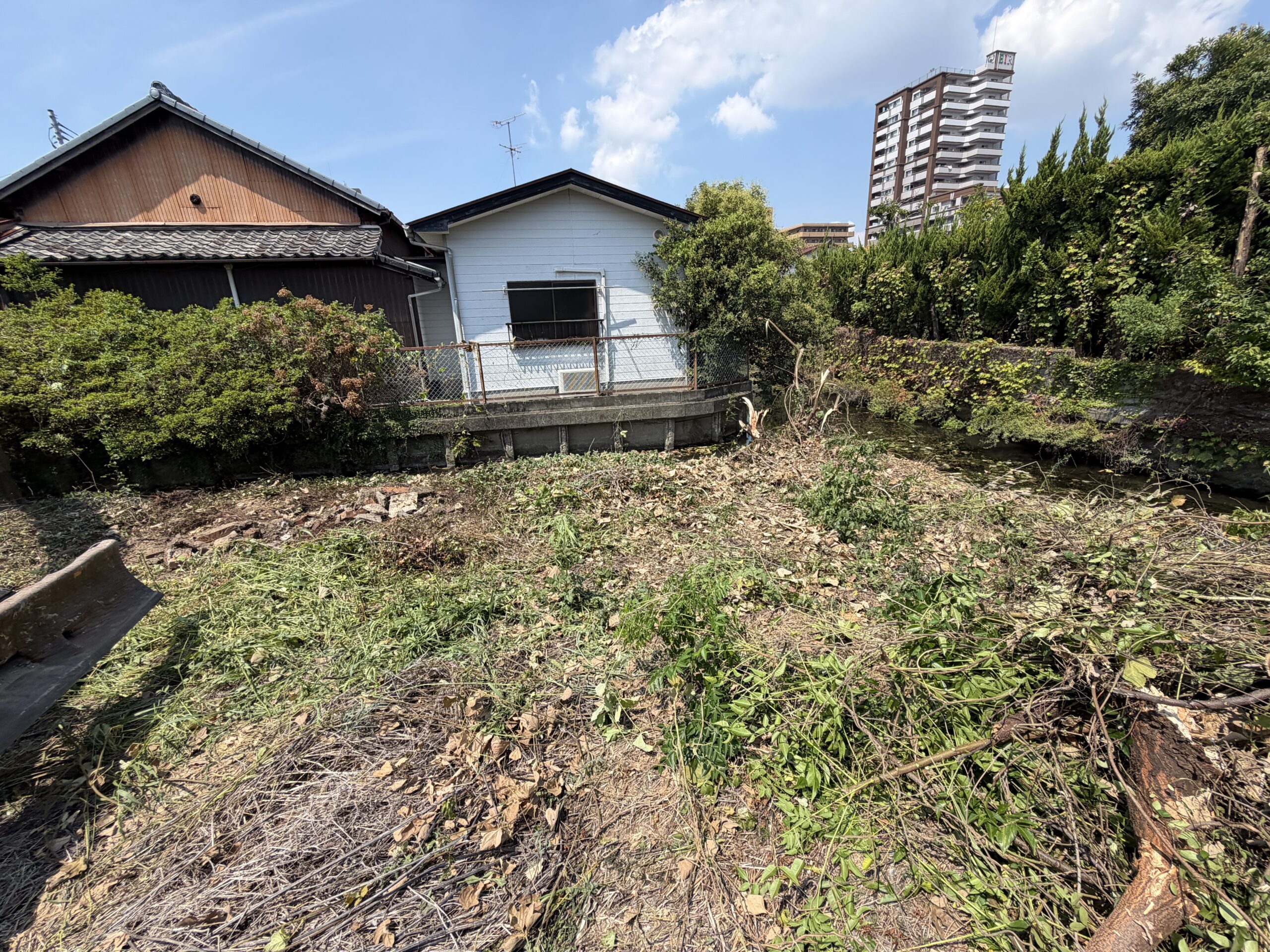 佐賀市水ケ江、伐採した草木を刈り集めた作業中の敷地と水路