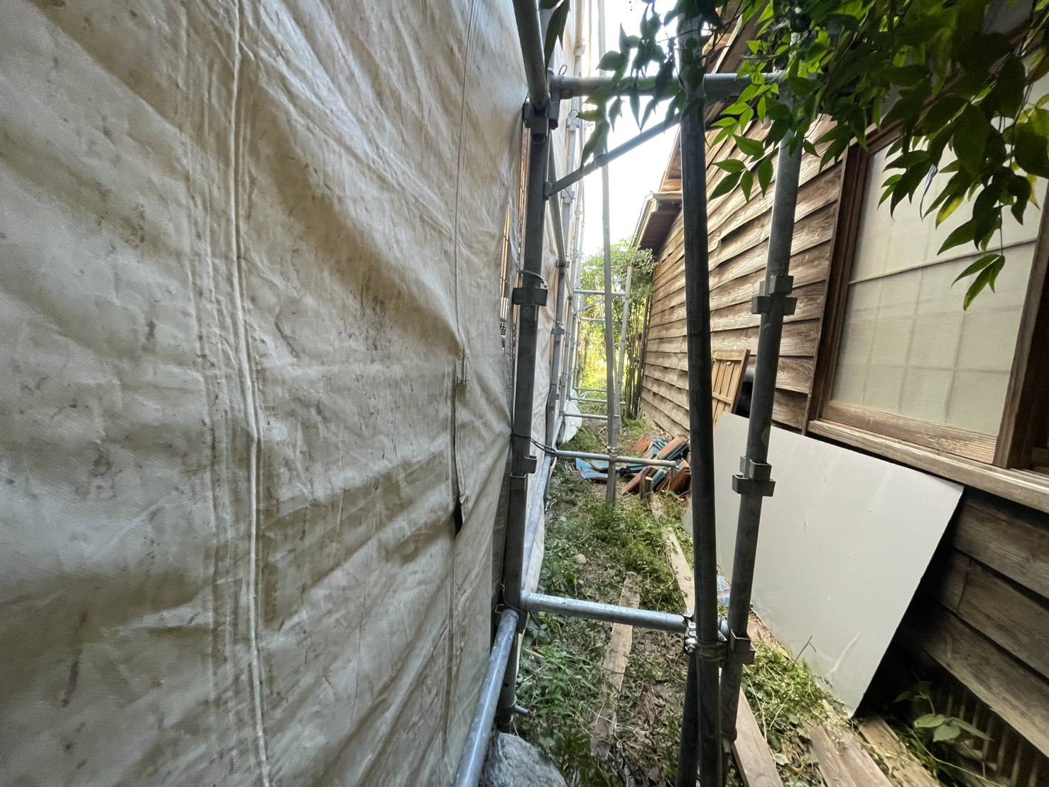 那珂川市松木、母屋と離れのあいだの狭い場所に組まれた足場と養生シート