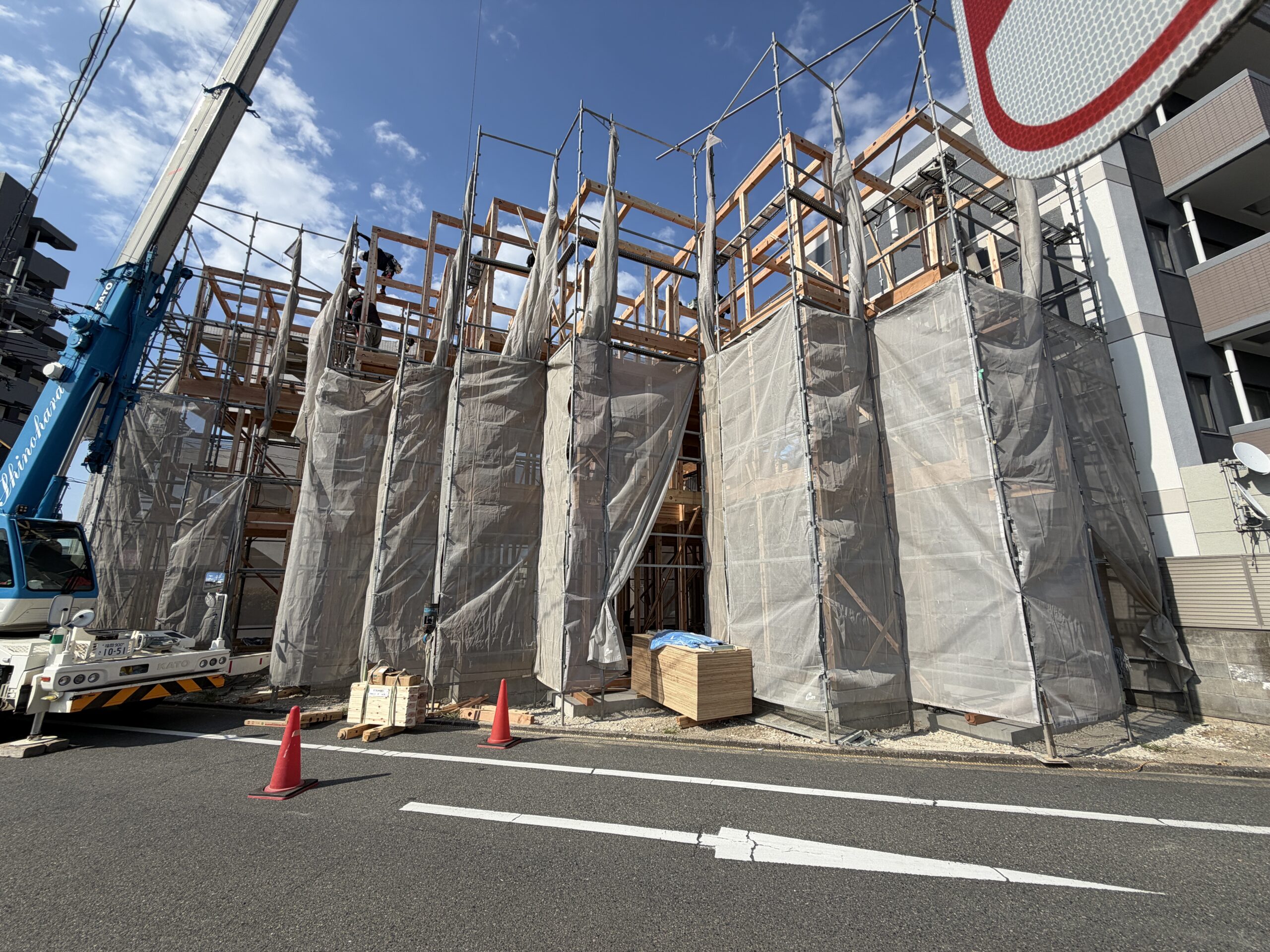 クレーンで木材を吊り上げ、建て方が進む今宿駅前の現場