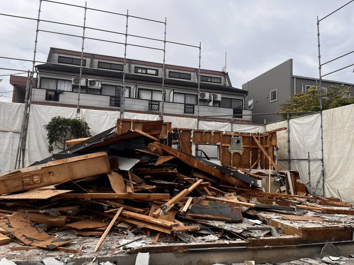 足場と養生シートに囲まれた敷地に横たわる、解体された木材