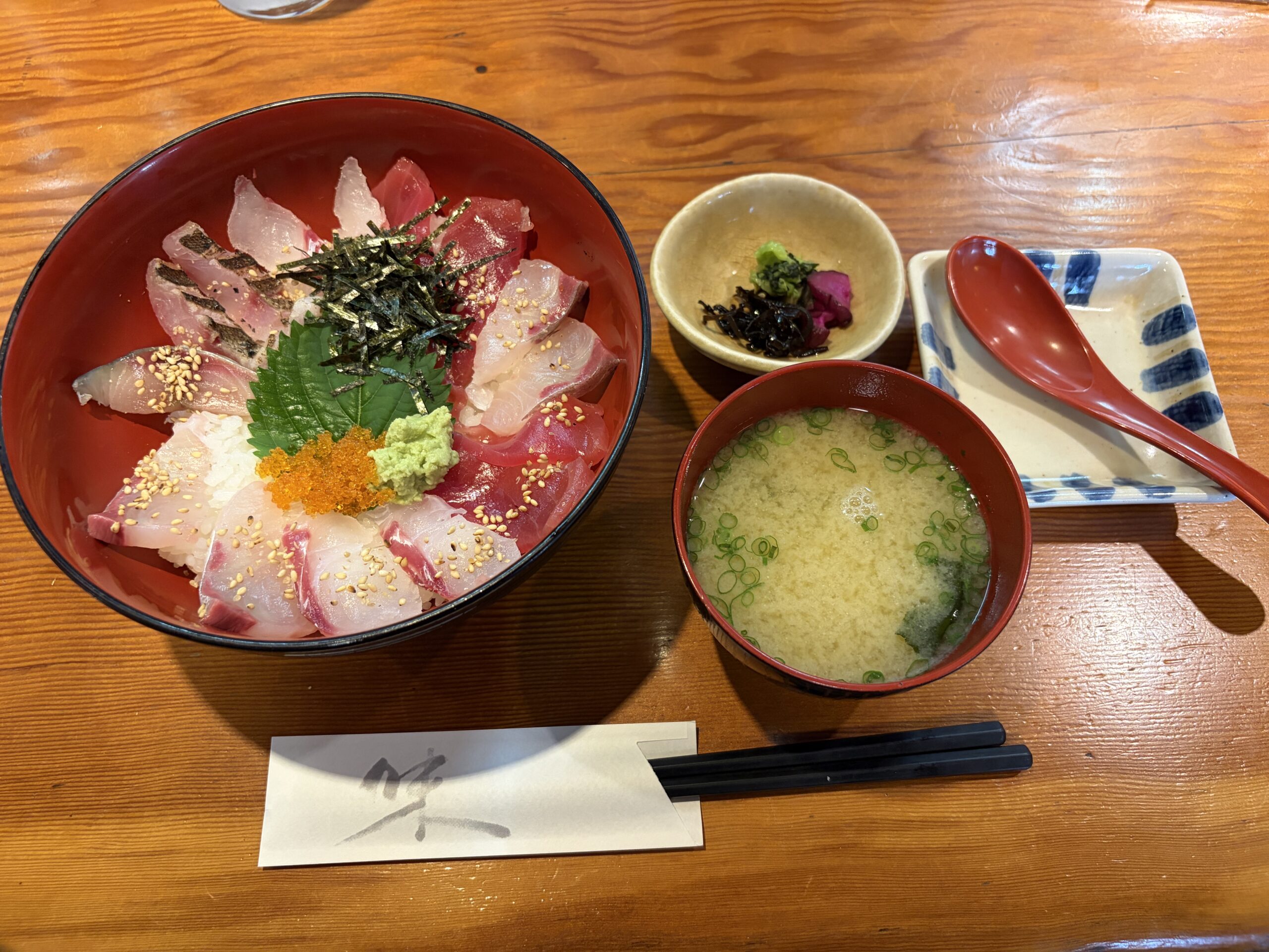 朱塗りのどんぶりに、白身と赤身のお刺身が並んだ海鮮丼。お味噌汁と小鉢が付いている