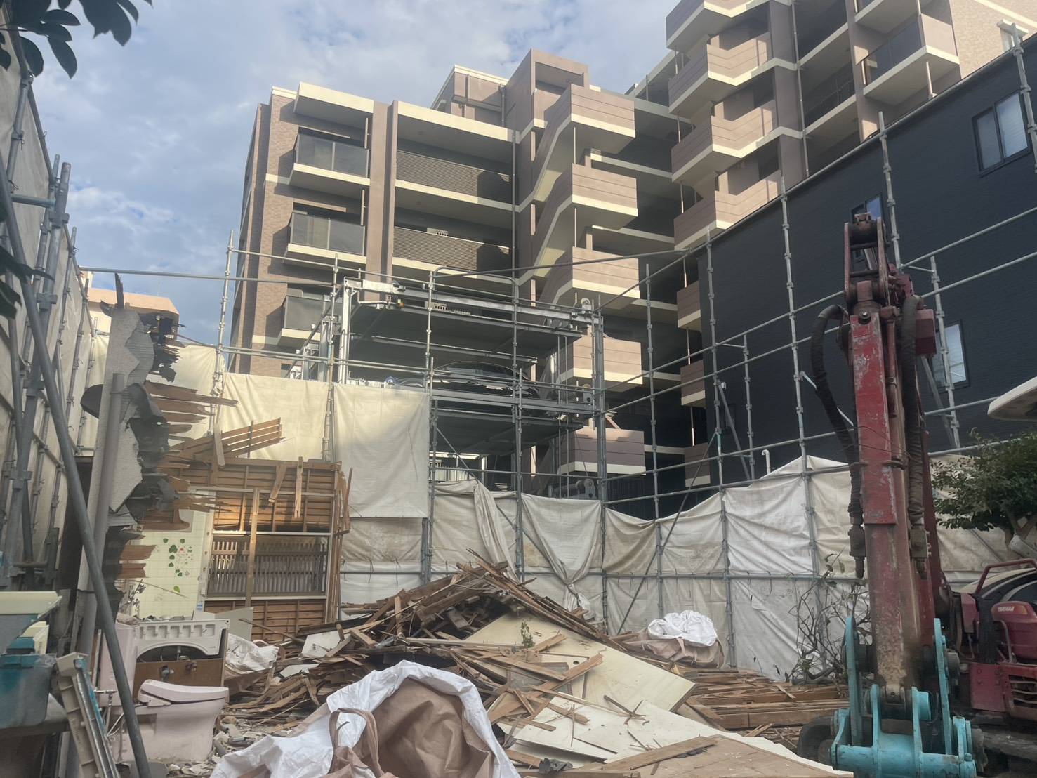 マンションを背に、足場とシートで囲った現場で作業する重機