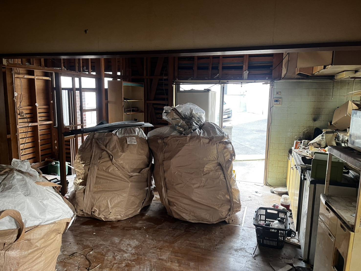 内装が外れて柱と骨組みが見える部屋と、床に並ぶ大きな袋