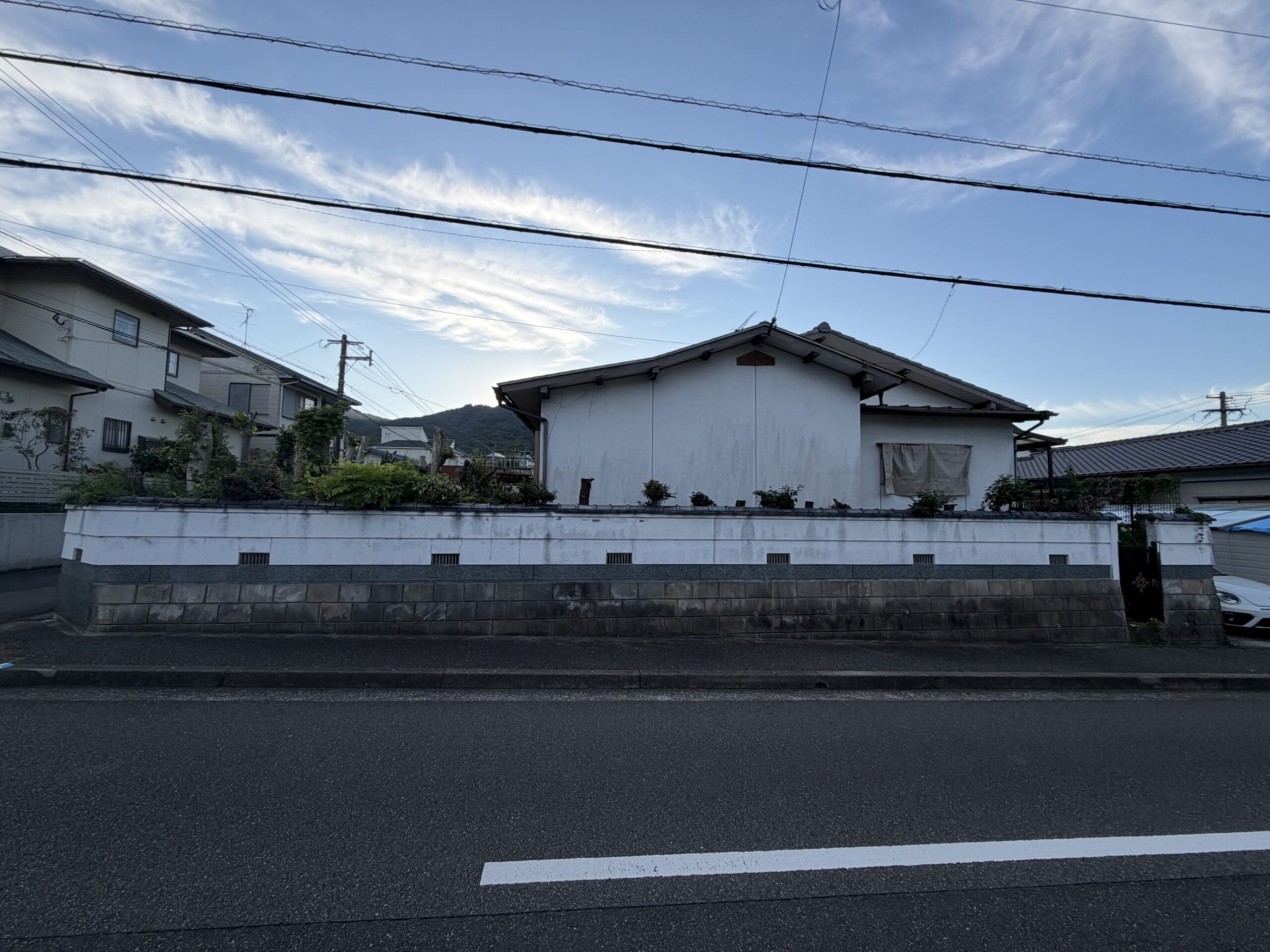 道路の向かいから見た、白い塀の奥に建つ瓦屋根の平屋