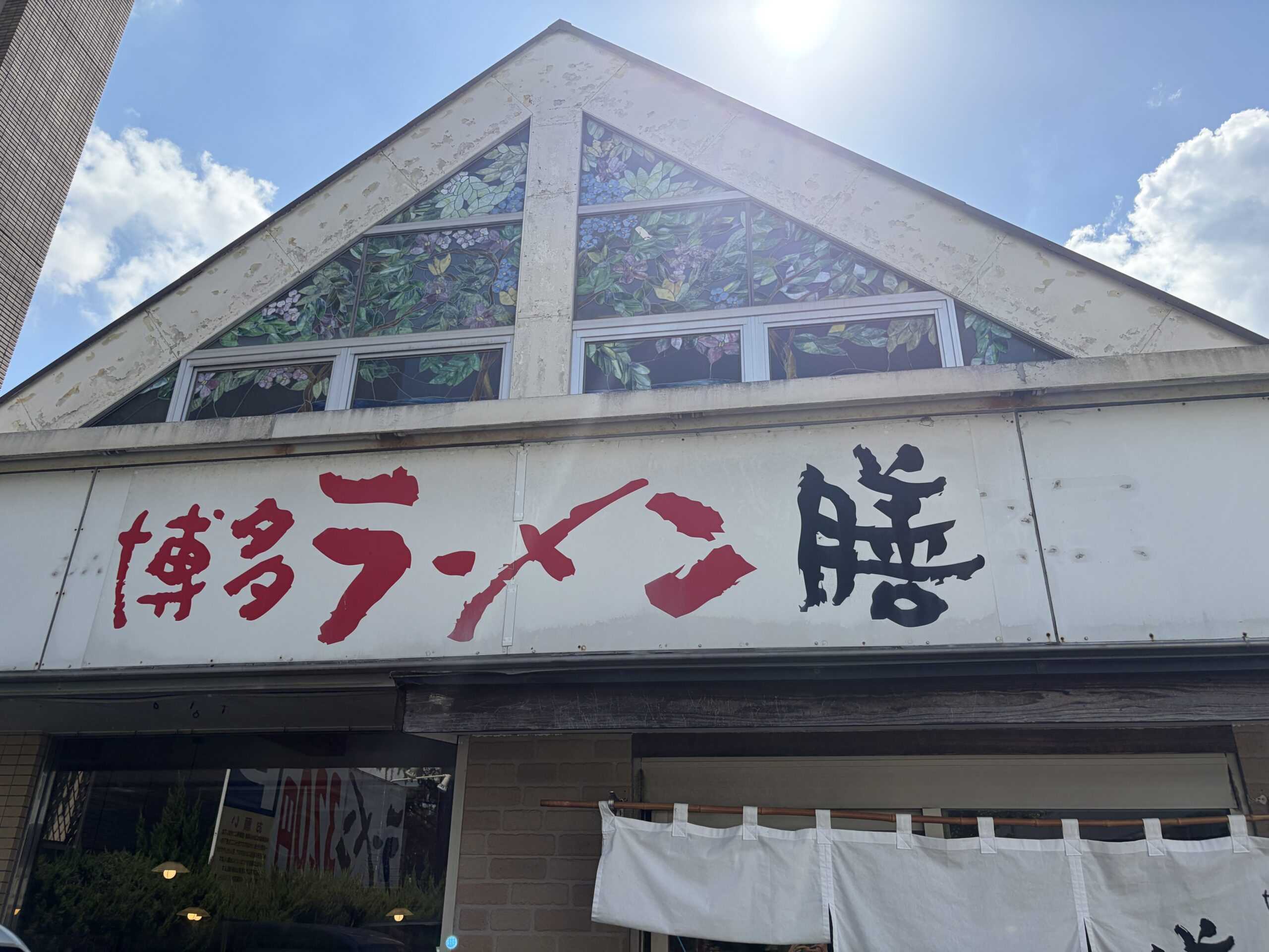 三角屋根の建物に掲げられた「博多ラーメン 膳」の看板と、白いのれん