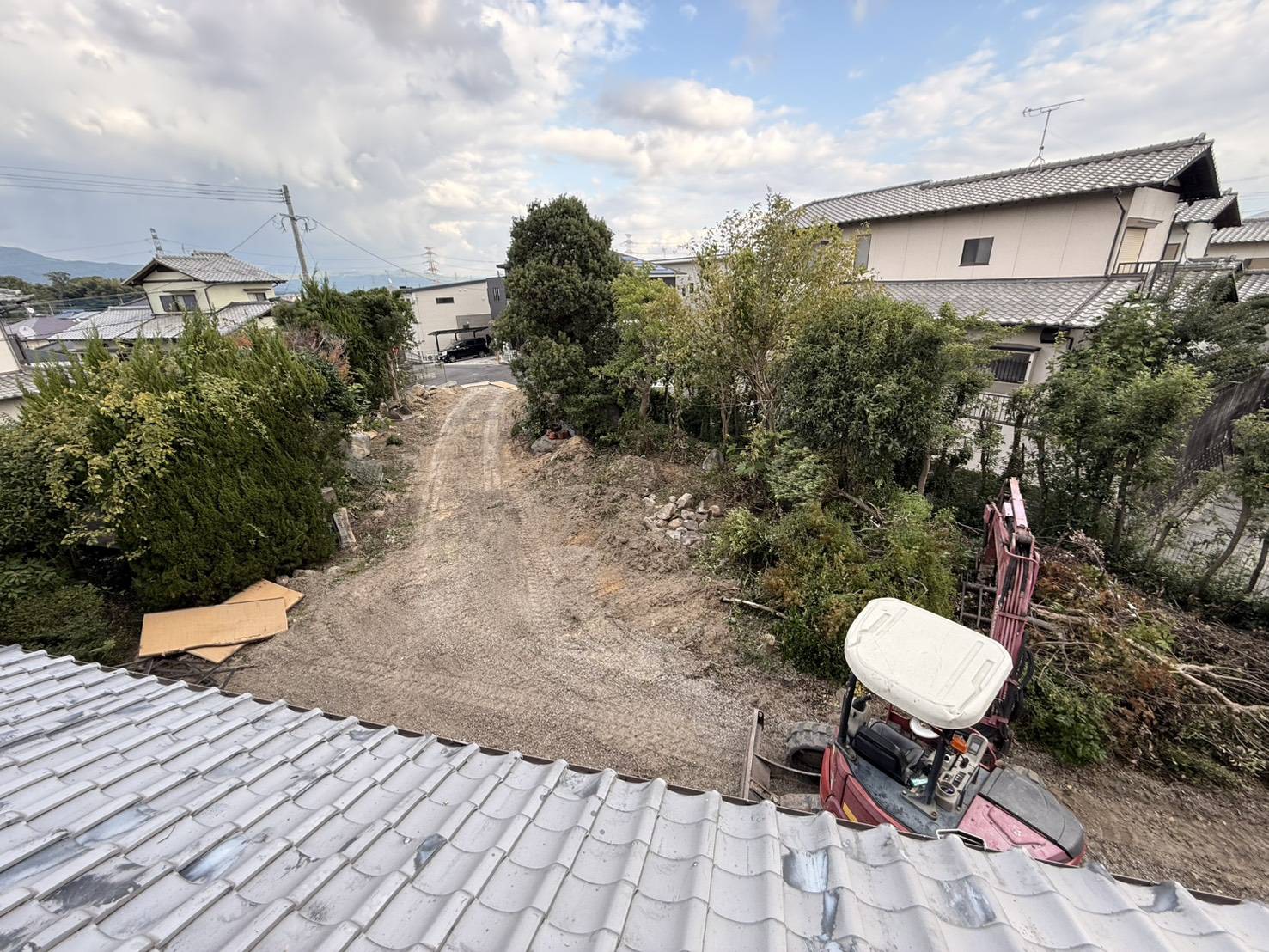 屋根の上から見た、木々に囲まれた庭と小型の重機