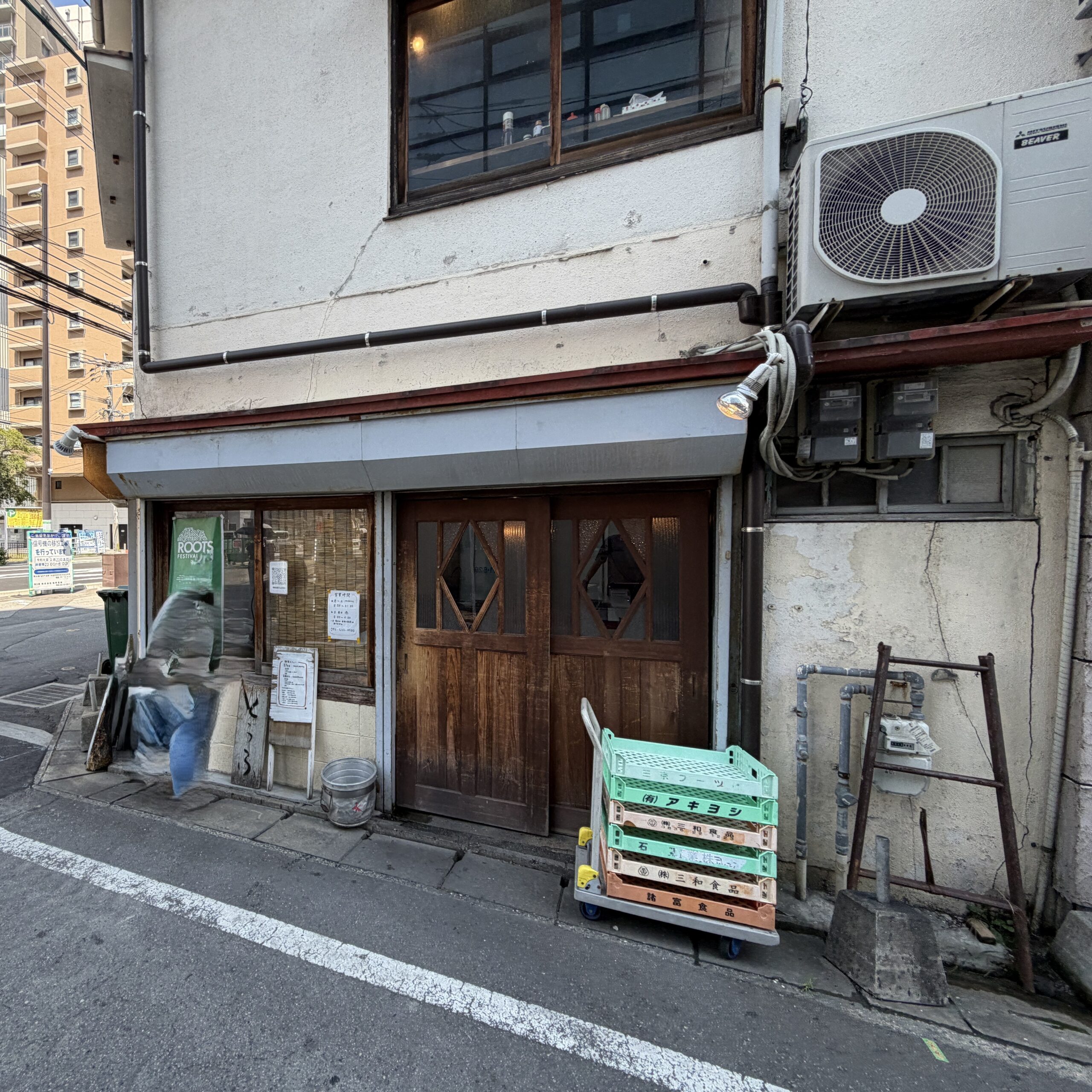 通りの向かい側から見た豆藤さんの建物と、その奥に建つマンション