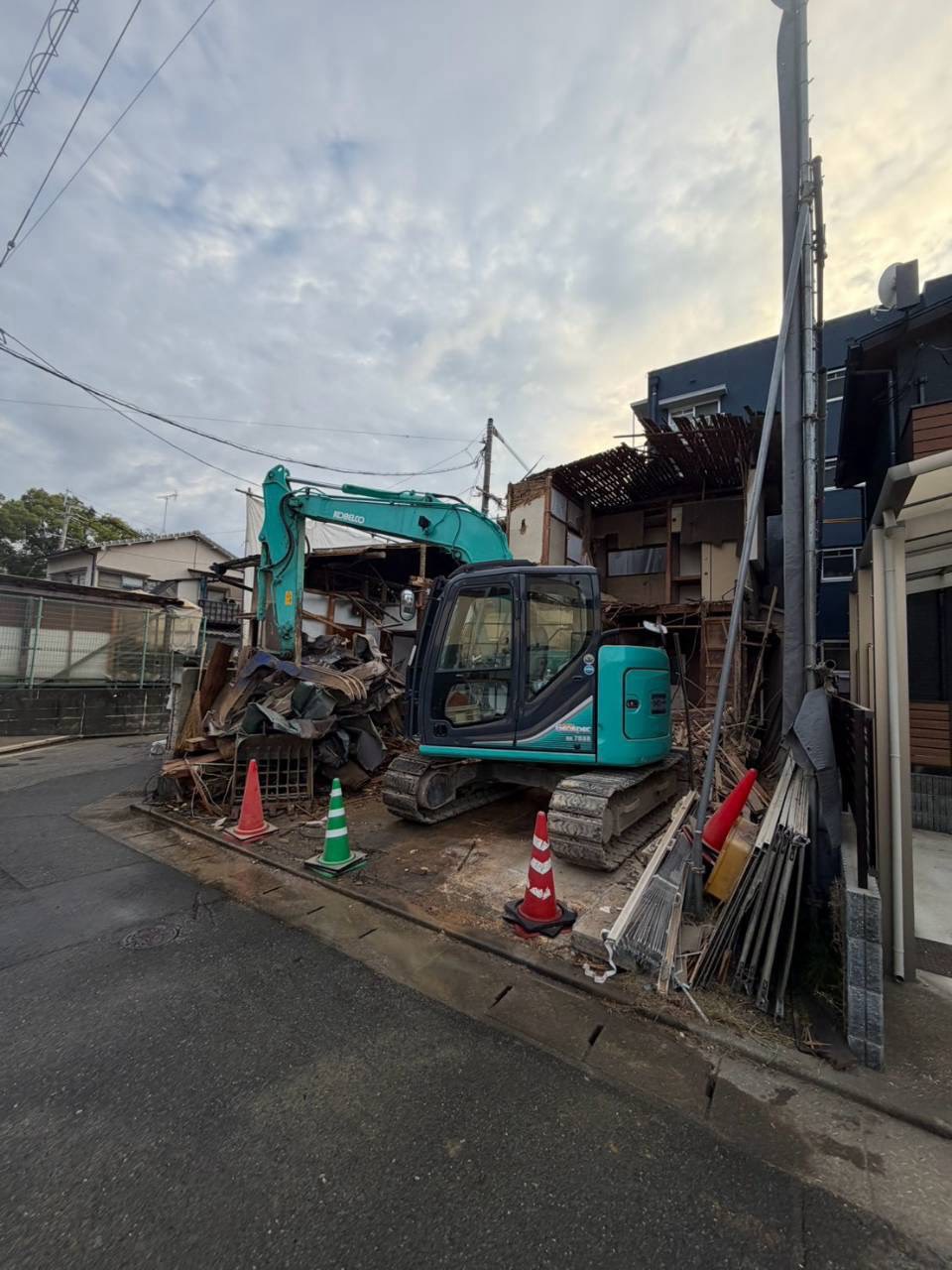 道路ぎわにコーンを並べ、重機で解体を進める現場