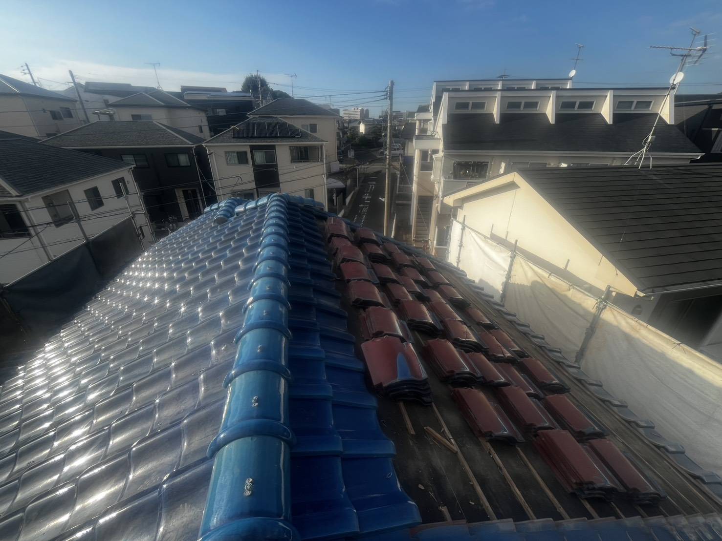 青い瓦の屋根。外した瓦が屋根の上に重ねられ、瓦の下の木が見えている