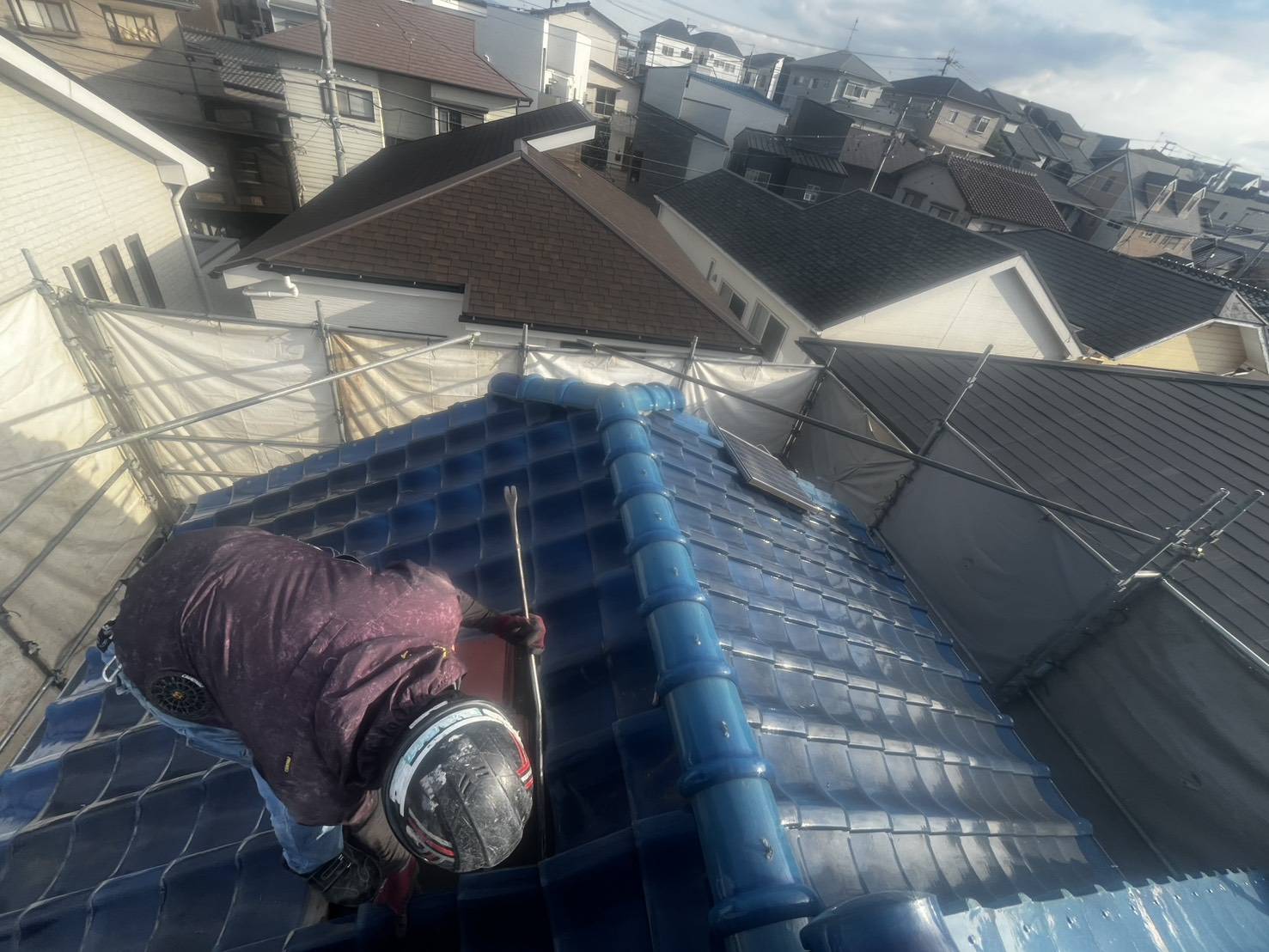 屋根の上で瓦を外す職人の後ろ姿